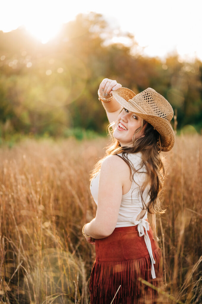 Smiling senior girl in a grassy field wearing a cowboy hat near Greensboro NC